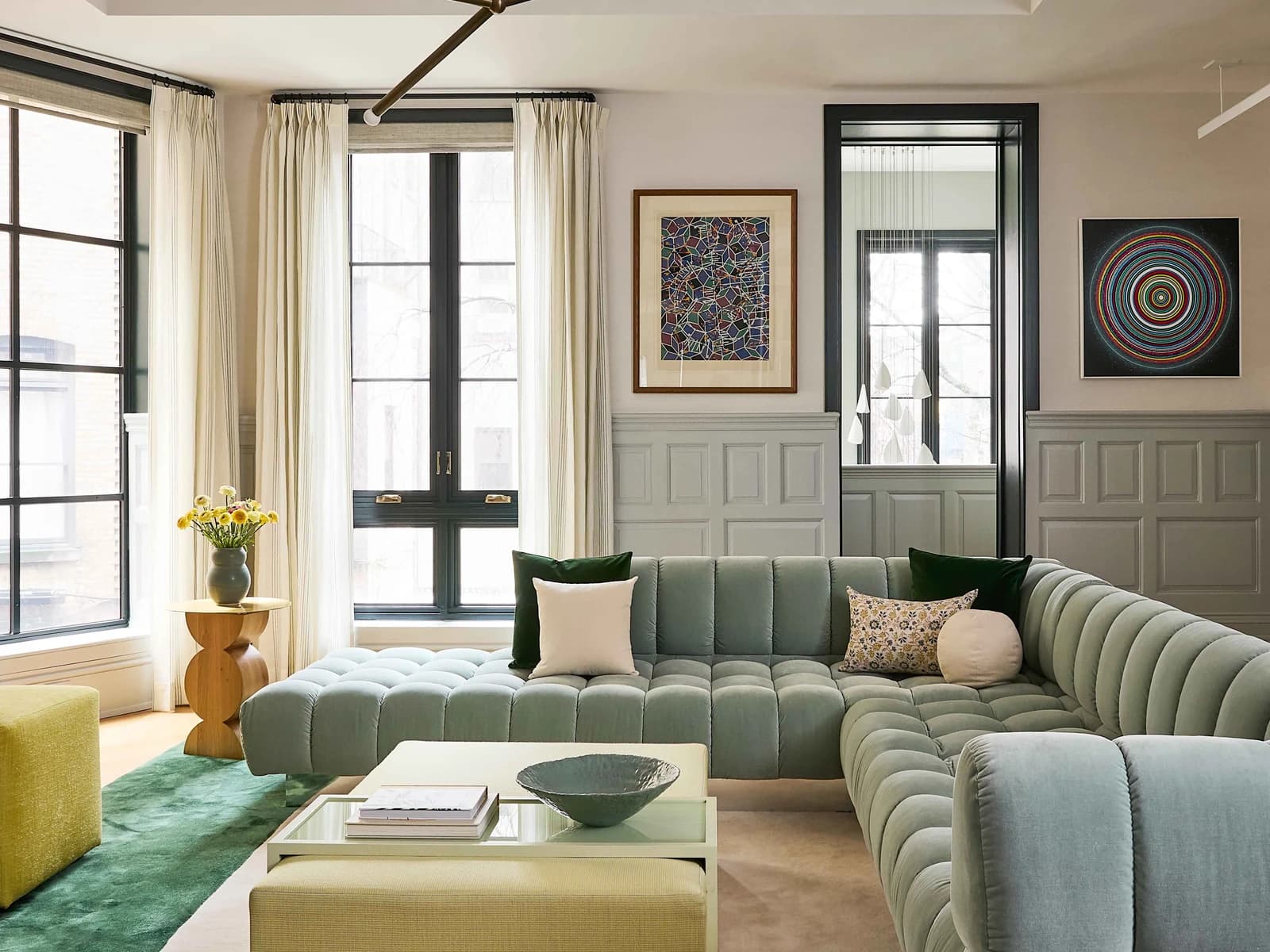 A living room with a curved sage green sofa, tall windows and panelled walls